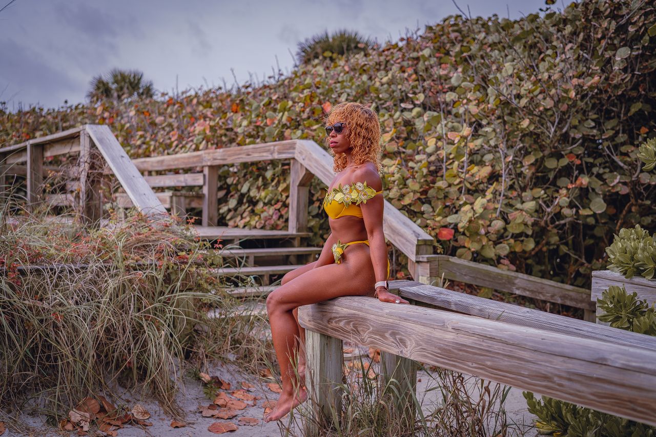 hero-img-01 African American woman in yellow bikini sitting on wooden bench outdoors.