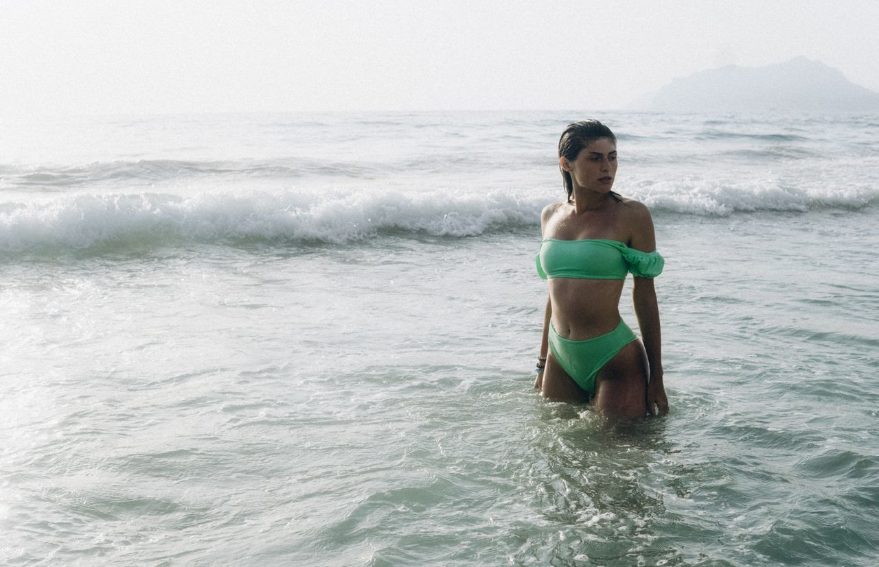 our-services-1 Woman in green bikini standing in the ocean waves on a sunny day.