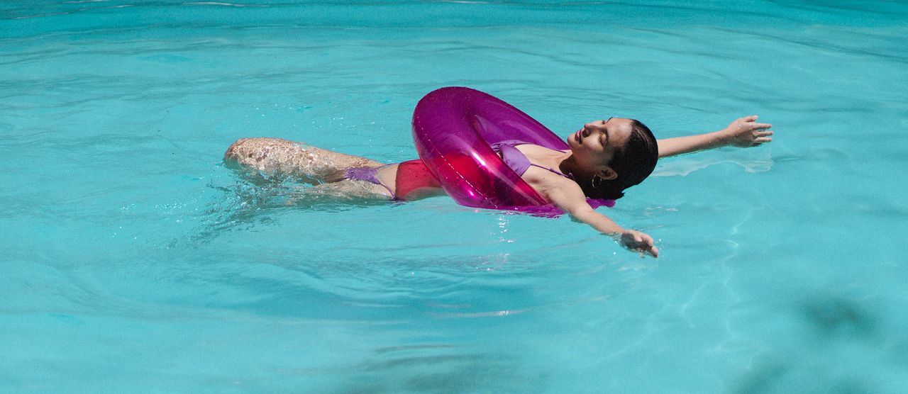why-choose-us Side view of positive young ethnic lady in swimwear lying on back in pool with rubber ring and sunbathing
